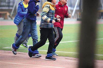 昨日，二外附小，学生绑着沙袋在跑步。有家长担心此举影响孩子发育，校方称旨在增强体质。新京报记者